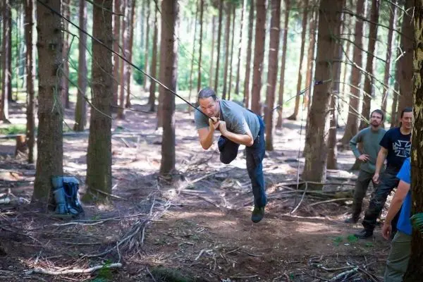 Mann überquert selbstgebaute Seilbrücke zwischen Bäumen im Wald