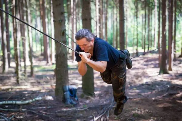 Mann überquert selbstgebaute Seilbrücke zwischen Bäumen im Wald