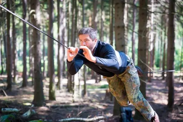 Mann überquert selbstgebaute Seilbrücke zwischen Bäumen im Wald