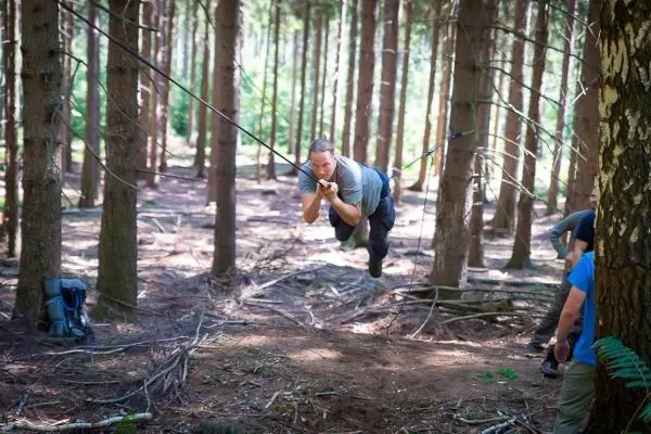 Mann überquert selbstgebaute Seilbrücke zwischen Bäumen im Wald