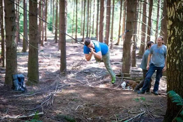 Mann überquert selbstgebaute Seilbrücke zwischen Bäumen im Wald