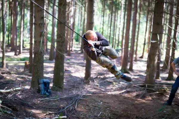 Mann überquert selbstgebaute Seilbrücke zwischen Bäumen im Wald