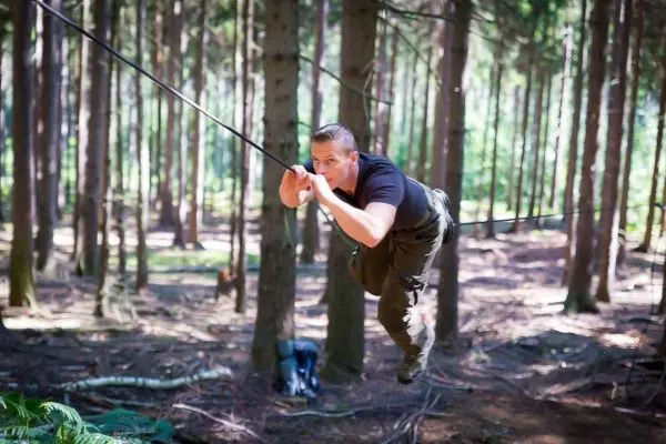 Mann überquert selbstgebaute Seilbrücke zwischen Bäumen im Wald