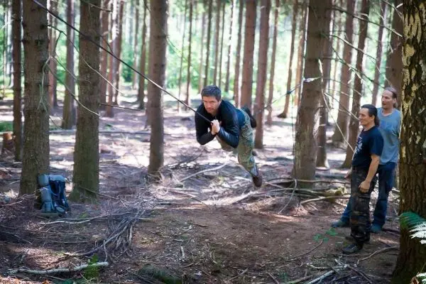 Mann überquert selbstgebaute Seilbrücke zwischen Bäumen im Wald