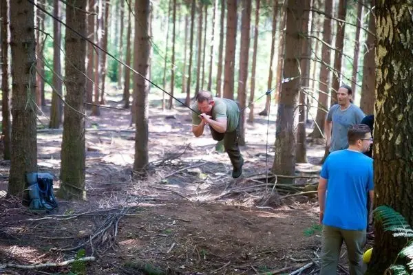 Mann überquert selbstgebaute Seilbrücke zwischen Bäumen im Wald