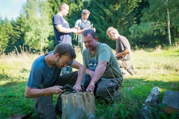 Messer bearbeitet Holzstamm, während andere Personen im Hintergrund arbeiten
