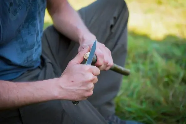 Messer schnitzt an einem Holzstück im Gras