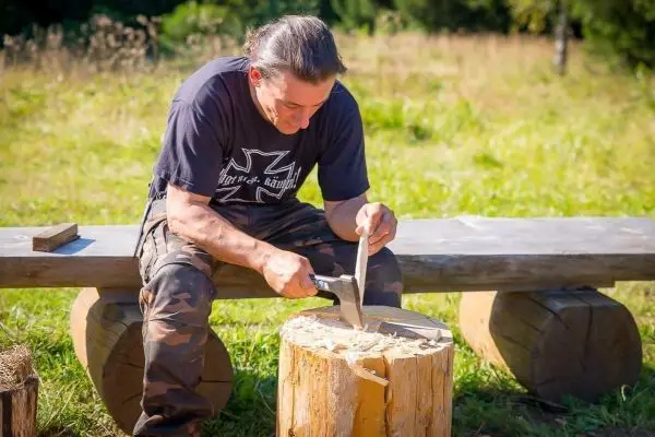 Messer schnitzt Holzstück auf einem Baumstamm im Freien
