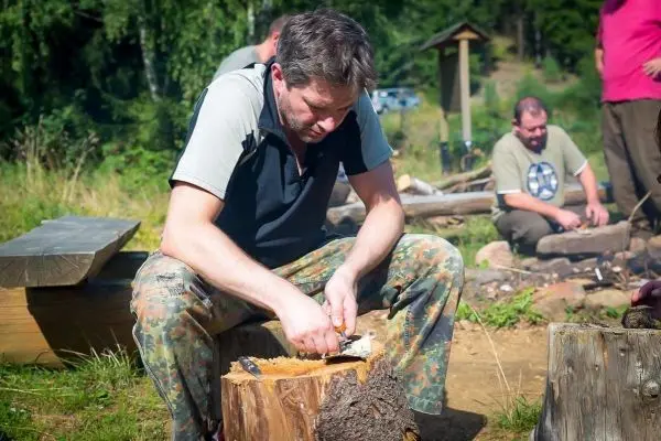 Messer schnitzt Zunder aus einem Holzstück auf einem Baumstumpf