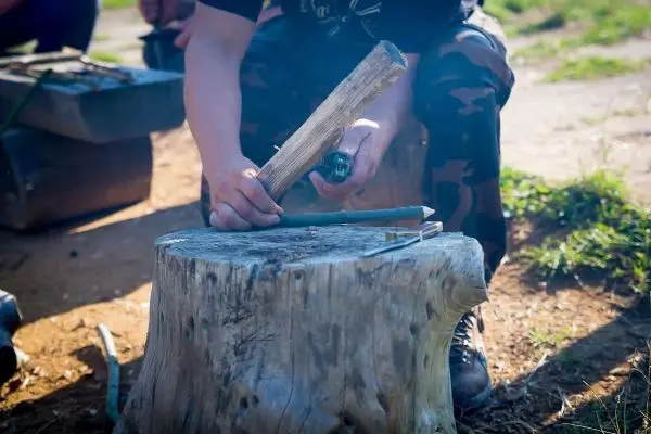 Person bearbeitet Holzstück auf einem Baumstumpf beim Überlebenstraining