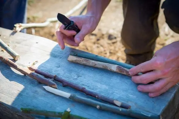Person bearbeitet Holzstücke mit einem Taschenmesser auf einem Tisch