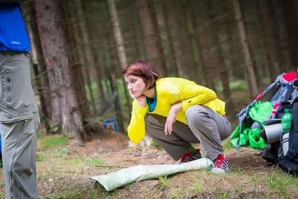 Person hockt neben einer ausgebreiteten Karte im Wald