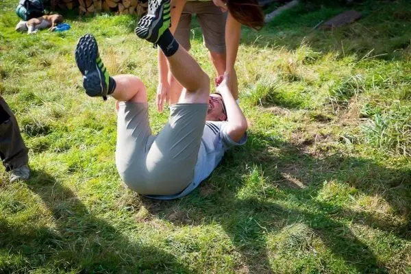 Person liegt auf dem Rücken im Gras, während eine andere Person ihn anhebt