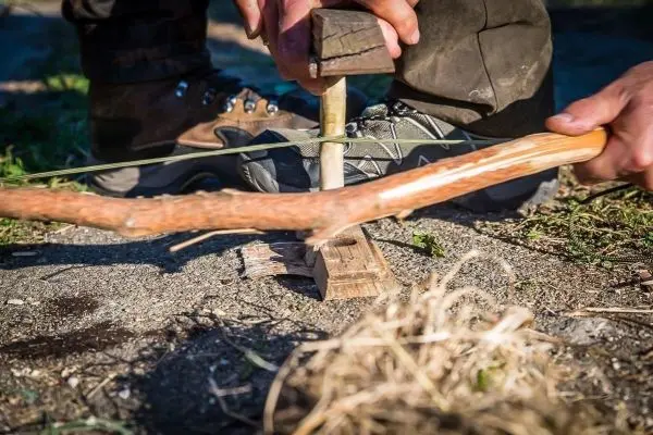 Person nutzt einen Stock zum Feuermachen im Freien