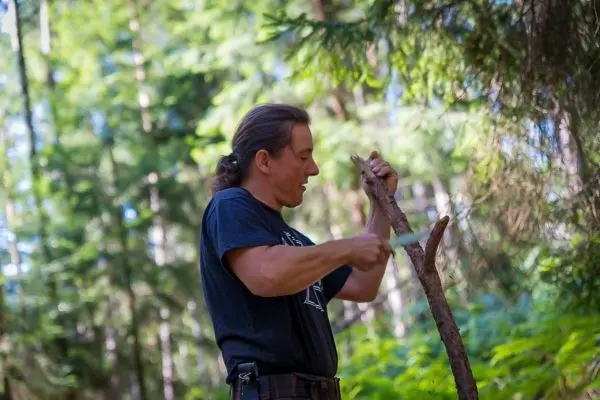 Person schnitzt mit einem Messer an einem Stock im Wald
