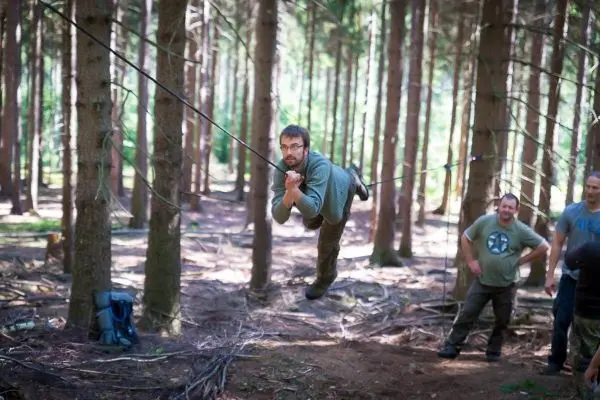 Person schwingt an einer selbstgebauten Seilbrücke durch den Wald