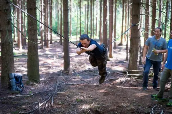 Person schwingt an einer selbstgebauten Seilbrücke durch den Wald