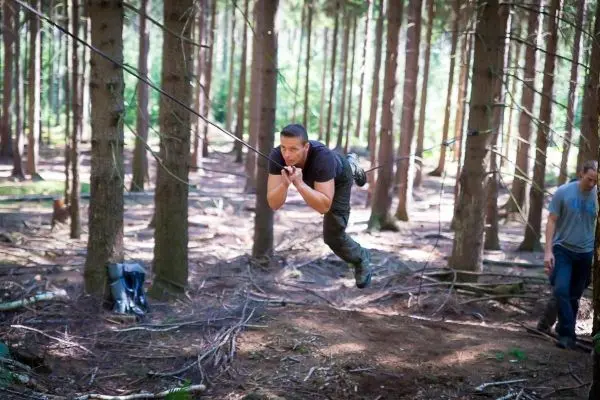 Person schwingt an Seil zwischen Bäumen im Wald beim Survival Training