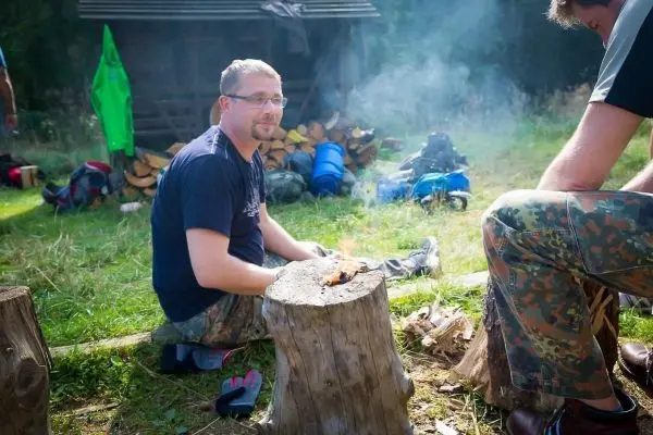 Person sitzt auf einem Baumstumpf und zündet Feuer an beim Survival Training