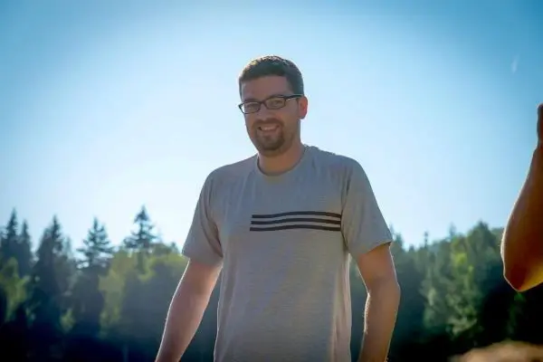 Person steht laechelnd im freien vor baeumen