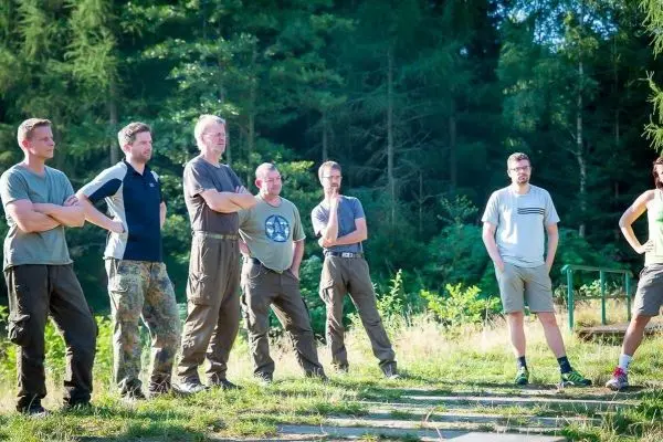 Sechs Personen stehen in einer Waldlichtung und beobachten eine Demonstration