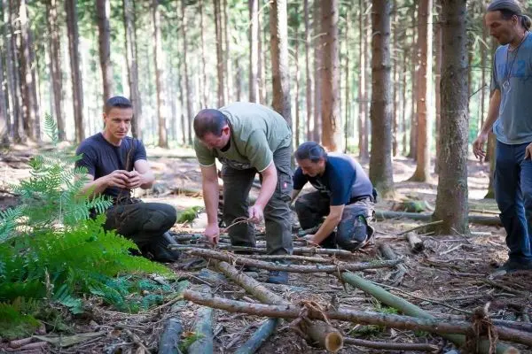 Vier Personen bauen eine Struktur aus Ästen im Wald