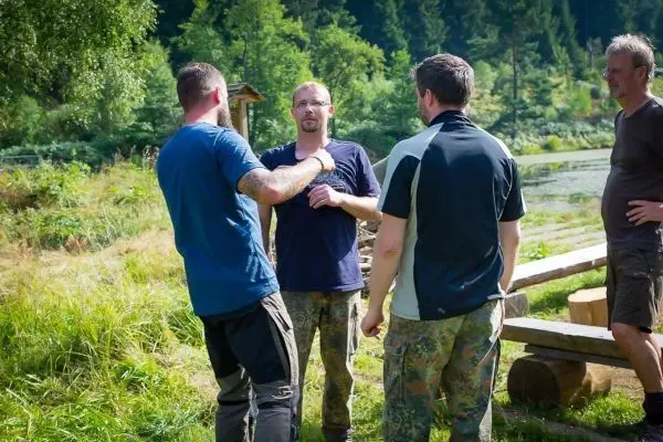 Vier Personen stehen im Gespräch auf einer Wiese neben Holzplanken