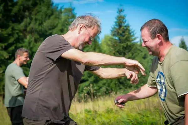 Zwei Männer üben eine Technik im Freien, während ein dritter im Hintergrund zuschaut