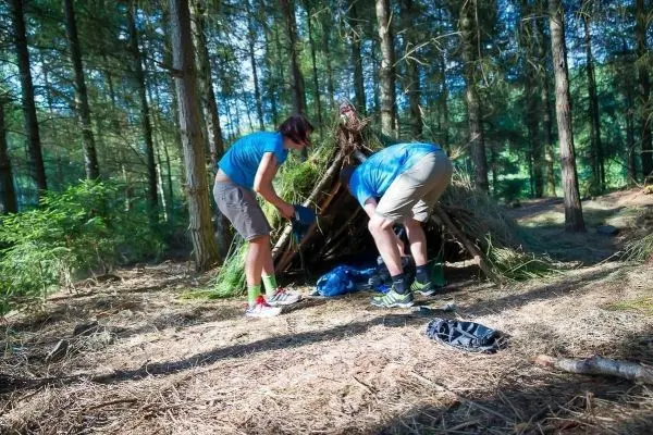 Zwei Personen bauen eine Tarp-Notunterkunft aus Ästen und Laub