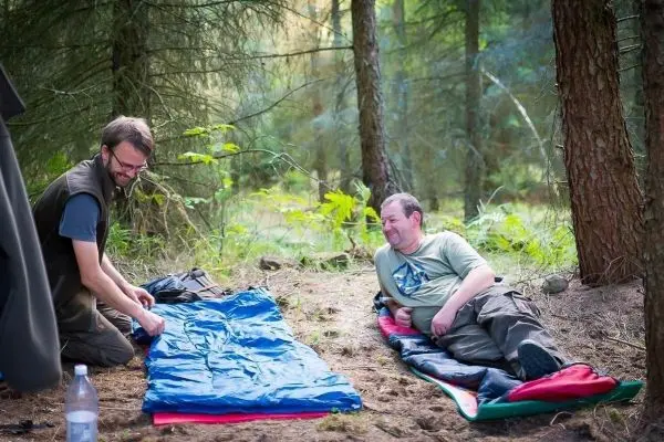 Zwei Personen bereiten Schlafsäcke im Wald für die Nacht vor