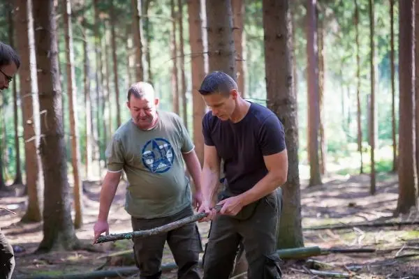 Zwei Personen halten gemeinsam einen langen Stock im Wald