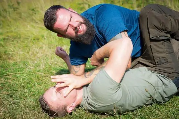 Zwei Personen im Bodenkampf auf Gras, einer hält den anderen fest