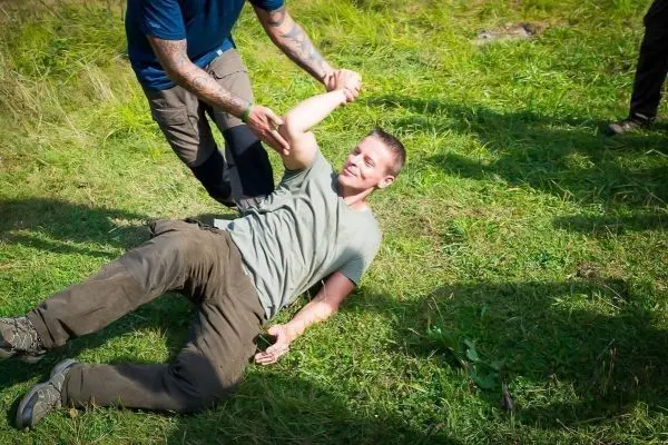 Zwei Personen interagieren auf einer Wiese, eine Person hält die andere am Arm