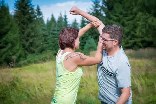 Zwei Personen interagieren spielerisch in einer grünen Wiese vor einem Wald