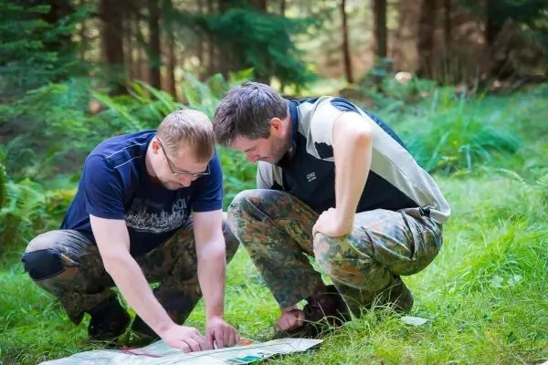 Zwei Personen knien im Wald und studieren eine Karte auf dem Boden