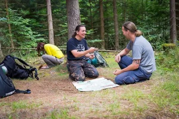 Zwei Personen sitzen auf dem Boden und betrachten eine Karte im Wald