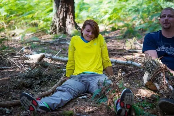 Zwei Personen sitzen im Wald auf dem Boden zwischen Ästen und Laub