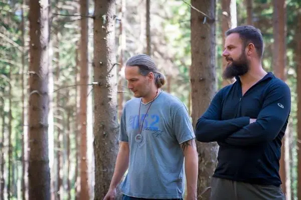 Zwei Personen stehen im Wald zwischen Bäumen und beobachten die Umgebung