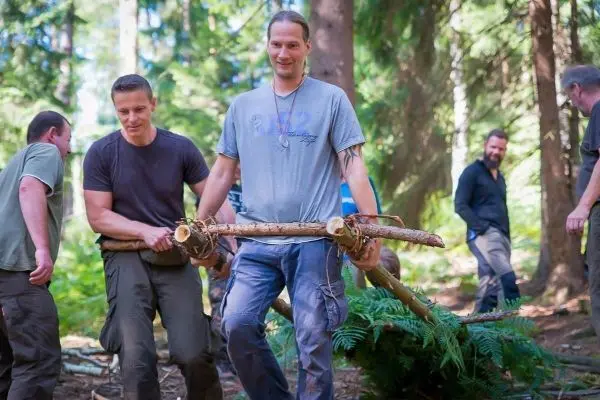Zwei Personen tragen eine selbstgebaute Trage aus Holzstöcken durch den Wald