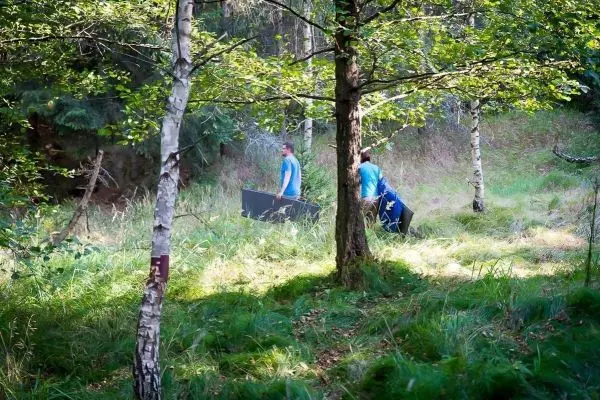 Zwei Personen tragen große Platten durch einen Wald mit hohem Gras