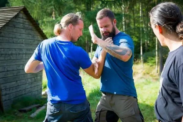 Zwei Personen üben eine Selbstverteidigungstechnik im Freien, während eine dritte Person zuschaut
