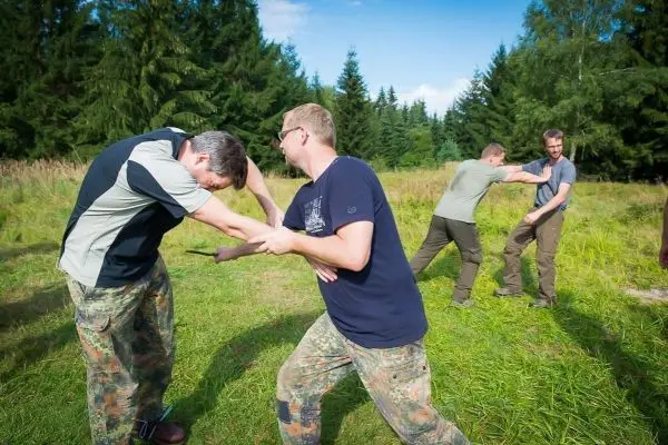Zwei Personen üben einen Nahkampf mit Holzstöcken in einer Wiese