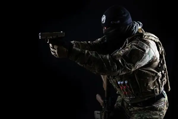 Bewaffnete Person zielt mit einer Handfeuerwaffe, trägt taktische Ausrüstung