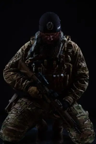 Soldat in Tarnkleidung kniet mit Gewehr in der Hand auf dem Boden