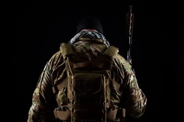 Soldat mit Rucksack und Gewehr, von hinten betrachtet, vor schwarzem Hintergrund