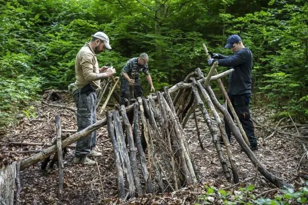 Drei Personen bauen eine Laubhütte aus Ästen im Wald