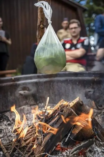 Ein Beutel mit grünem Inhalt hängt über einem Feuer