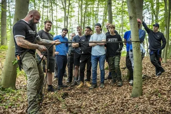 Ein Mann demonstriert das Binden eines Knotens mit einem Seil zwischen zwei Bäumen