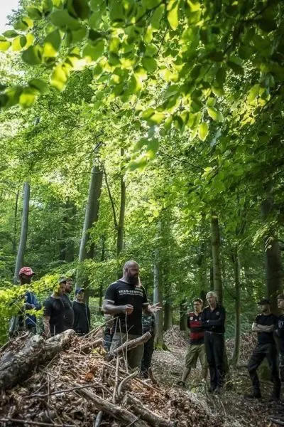 Ein Mann erklärt Techniken im Wald, umgeben von Zuhörern und Bäumen