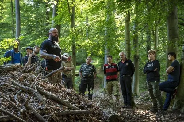 Ein Mann erklärt Techniken zur Naturüberleben vor einer Gruppe im Wald